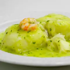 Merluza en salsa verde, un plato tradicional con trozos de pescado blanco y un camarón encima, bañado en una deliciosa salsa verde.