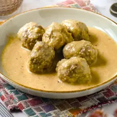 Deliciosas albóndigas en salsa de almendras, servidas en un plato sobre un mantel colorido.