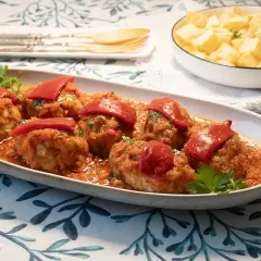 Sabrosos **rollos de bonito** en salsa de tomate, coronados con pimientos rojos. Acompañados de patatas fritas en un bol.