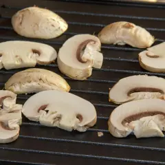 Champiñones cortados a la mitad y enteros sobre una parrilla, listos para deliciosas recetas con champiñones.