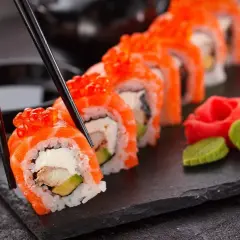 Palillos recogen un rollo de sushi con salmón y huevas de salmón, listo para disfrutar. Aprende como hacer sushi.
