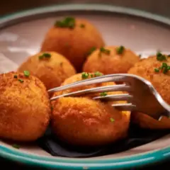 Croquetas de puchero doradas y crujientes, servidas en un plato con un tenedor listo para probarlas.