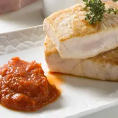 Dos jugosos trozos de atún a la plancha, con sal gruesa y una ramita de tomillo, acompañados de una porción de salsa de tomate casera.