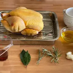 Un pollo crudo listo para asar, con ingredientes como limón, aceite, hierbas, ajo y sal. ¡Perfecto para un delicioso pollo al ast!