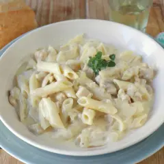 Un plato cremoso de macarrones con nata y trocitos de pollo, decorado con una ramita de tomillo.