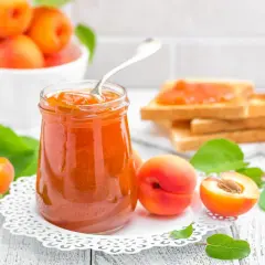 Tarro de mermelada de albaricoque casera, con tostadas y albaricoques frescos alrededor.