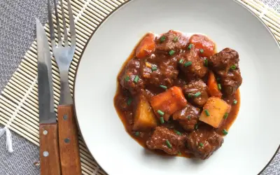 Un plato de goulash de ternera con trozos de patata y zanahoria, adornado con cebollino. Cubiertos de una rica salsa.