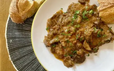 Plato de fricando de ternera con salsa cremosa y trozos de pan crujiente.