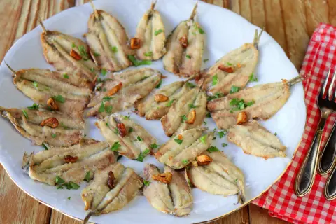 Boquerones en freidora de aire, dorados y crujientes, servidos en plato blanco con perejil picado y ajos fritos. ¡Un manjar saludable!