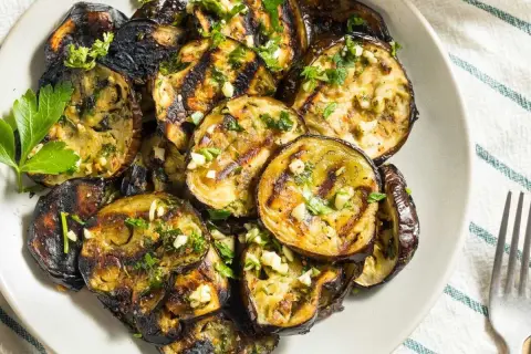 Rodajas de berenjenas a la plancha, doradas y tiernas, con ajo picado y perejil fresco. Un plato sencillo y delicioso.