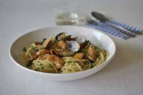 Un plato de spaghetti frutti di mare con gambas, mejillones y almejas, adornado con perejil fresco.