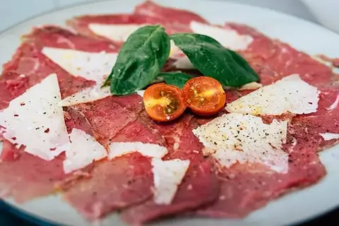 Carpaccio de ternera con queso parmesano, hojas de albahaca y tomates cherry cortados por la mitad.