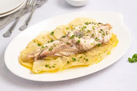 Rape al horno servido sobre patatas laminadas y espolvoreado con perejil fresco. Un plato sencillo y delicioso.