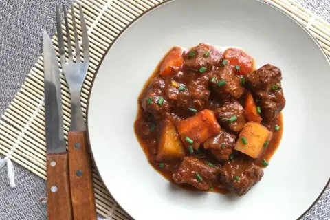 Un plato de goulash de ternera con trozos de patata y zanahoria, adornado con cebollino. Cubiertos de una rica salsa.