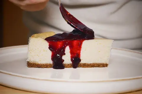 Un trozo de new york cheesecake cremoso con salsa de frutos rojos cayendo.