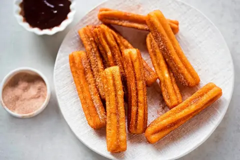 Churros sin gluten espolvoreados con azúcar y canela, servidos con chocolate caliente.