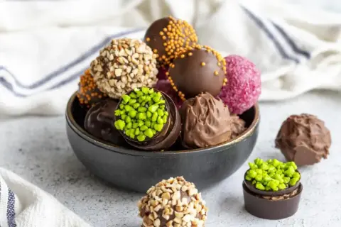Un tazón lleno de deliciosas trufas de chocolate, algunas cubiertas de frutos secos, otras con chispas de colores y pistachos.