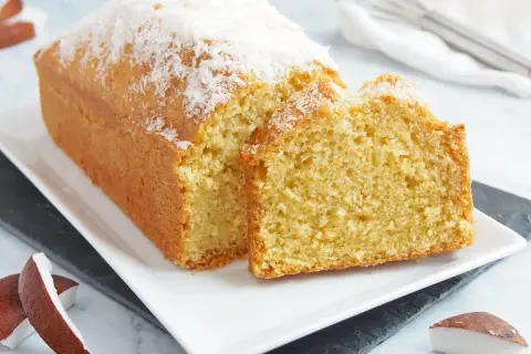 Bizcocho de coco esponjoso, cubierto con coco rallado, servido en una bandeja blanca.