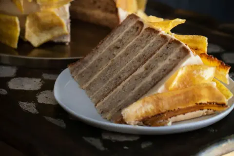 Rebanada de tarta de plátano con capas de bizcocho y crema, decorada con trozos de plátano caramelizado.