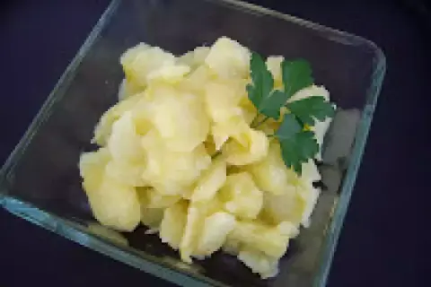 Un cuenco de cristal contiene patatas al montón, un plato sencillo y reconfortante, adornado con una ramita de perejil fresco.
