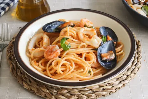 Un plato de espaguetis a la marinera con gambas, calamares y mejillones, servido en un cuenco sobre una esterilla de mimbre.