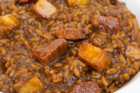 Un plato de arroz con acelgas y trozos de carne en una salsa oscura y apetitosa.
