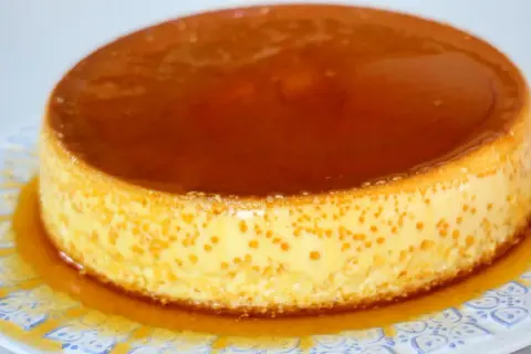 Delicioso flan de queso Philadelphia con caramelo líquido, servido en un plato blanco con diseño azul.
