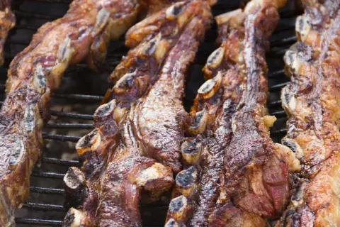 Costillas de churrasco a la plancha, doradas y jugosas, cocinándose lentamente sobre la parrilla.