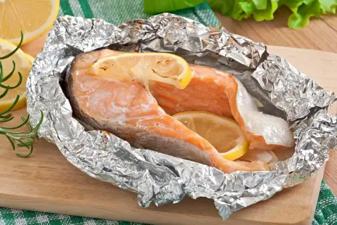 Salmón jugoso en papel de aluminio con rodajas de limón y romero.