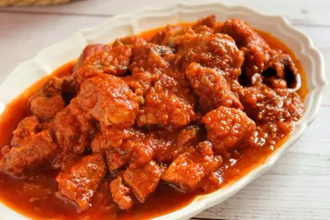 Magro con tomate en un plato blanco, con trozos de carne en salsa roja.