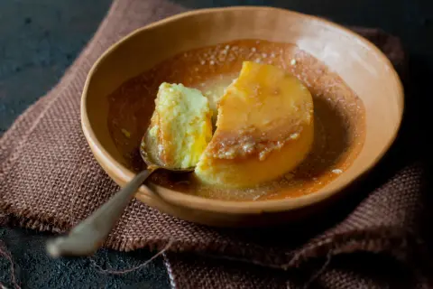 Un trozo de flan de yogur cremoso, bañado en caramelo líquido, servido en un cuenco de barro.