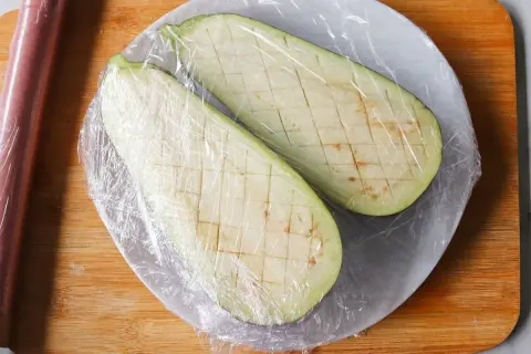 Dos mitades de berenjena cortadas en cubos y cubiertas con plástico, listas para cocinar berenjenas al microondas.