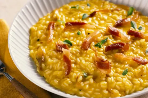Cremoso risotto de queso, con trozos de panceta crujiente y hojas verdes.
