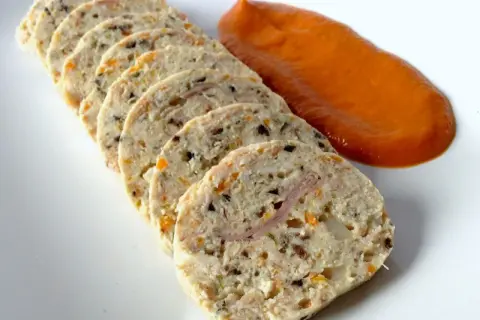 Fiambre de pollo casero en rodajas, con trocitos de verdura y jamón, acompañado de una salsa naranja.
