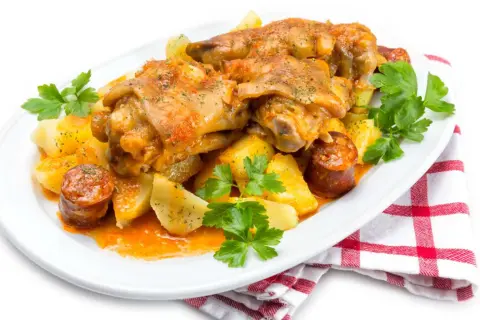 Manitas de cerdo receta tradicional de la abuela, con patatas y chorizo, servido en plato blanco con perejil fresco.