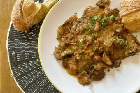 Plato de fricando de ternera con salsa cremosa y trozos de pan crujiente.