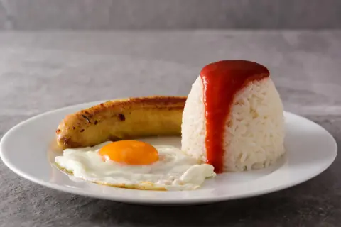 Un plato de arroz a la cubana con huevo frito y salchicha, cubierto con salsa de tomate.