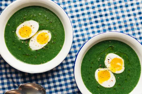 Dos cuencos de espinacas a la crema con huevos duros cortados por la mitad, servidos sobre un mantel de cuadros azules y blancos.