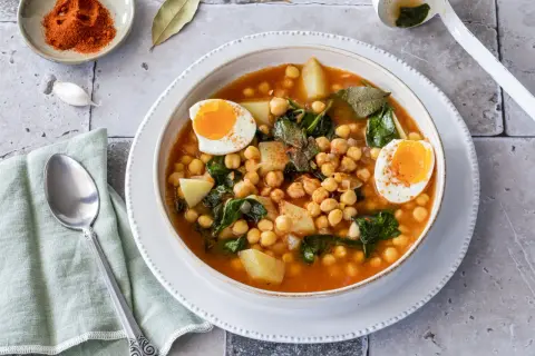 Un reconfortante plato de garbanzos con espinacas, patatas y huevos cocidos, espolvoreado con pimentón.