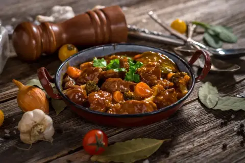 Caldereta de cordero humeante, con trozos de carne tierna, zanahoria y brócoli, servida en una cazuela rústica.