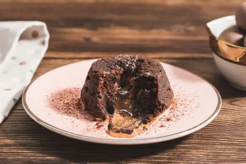 Coulant de chocolate con centro líquido y cremoso, espolvoreado con cacao en polvo sobre un plato rosa.