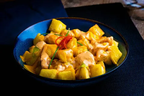 Patatas bravas receta: trozos dorados de patata cubiertos con una cremosa salsa rosada y decorados con pimiento rojo y cebollino.