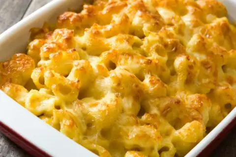 Mac and cheese cremoso y dorado, recién salido del horno en una fuente roja.