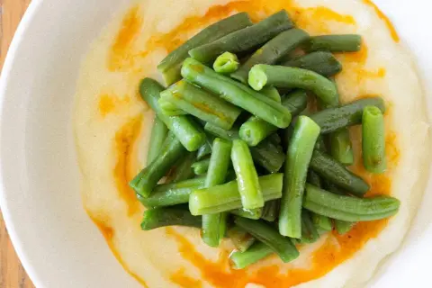 Judías verdes frescas y tiernas sobre un puré cremoso, con un toque de aceite de pimentón. Un plato sencillo y delicioso de judías verdes con patatas.