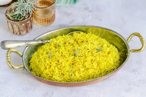 Un aromático arroz al curry, teñido de un vibrante amarillo por la cúrcuma y decorado con hebras de azafrán y romero fresco.