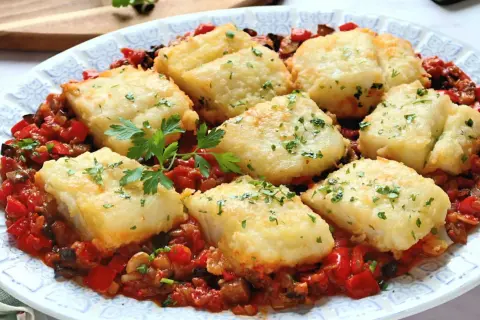 Bacalao con sanfaina: trozos de pescado blanco rebozado sobre una cama de pimientos rojos, berenjena y tomate.