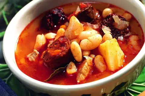 Un reconfortante plato de alubias con chorizo, trozos de morcilla y patatas en un cuenco blanco.