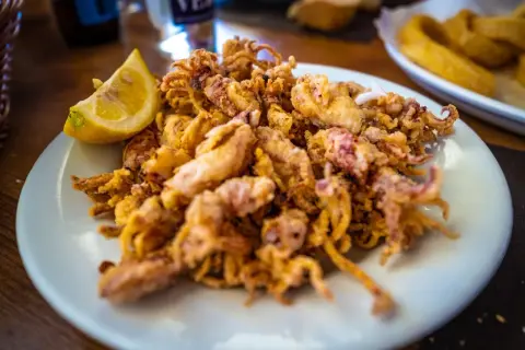 Plato de puntillas de calamar fritas, crujientes y doradas, servido con una rodaja de limón.