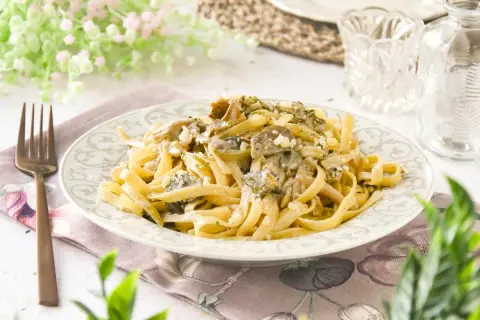 Pasta con setas cremosa, servida en un plato decorado, con un tenedor de bronce al lado.