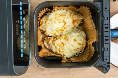Dos berenjenas rellenas, cubiertas de queso derretido y dorado, listas para disfrutar tras su paso por la freidora de aire.